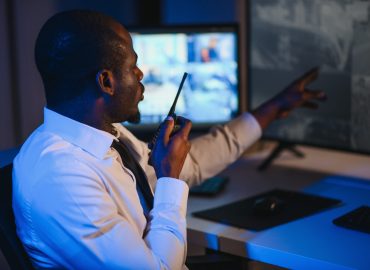 African-american,Security,Officer,Watching,The,Screens,Talking,On,Radio,In
